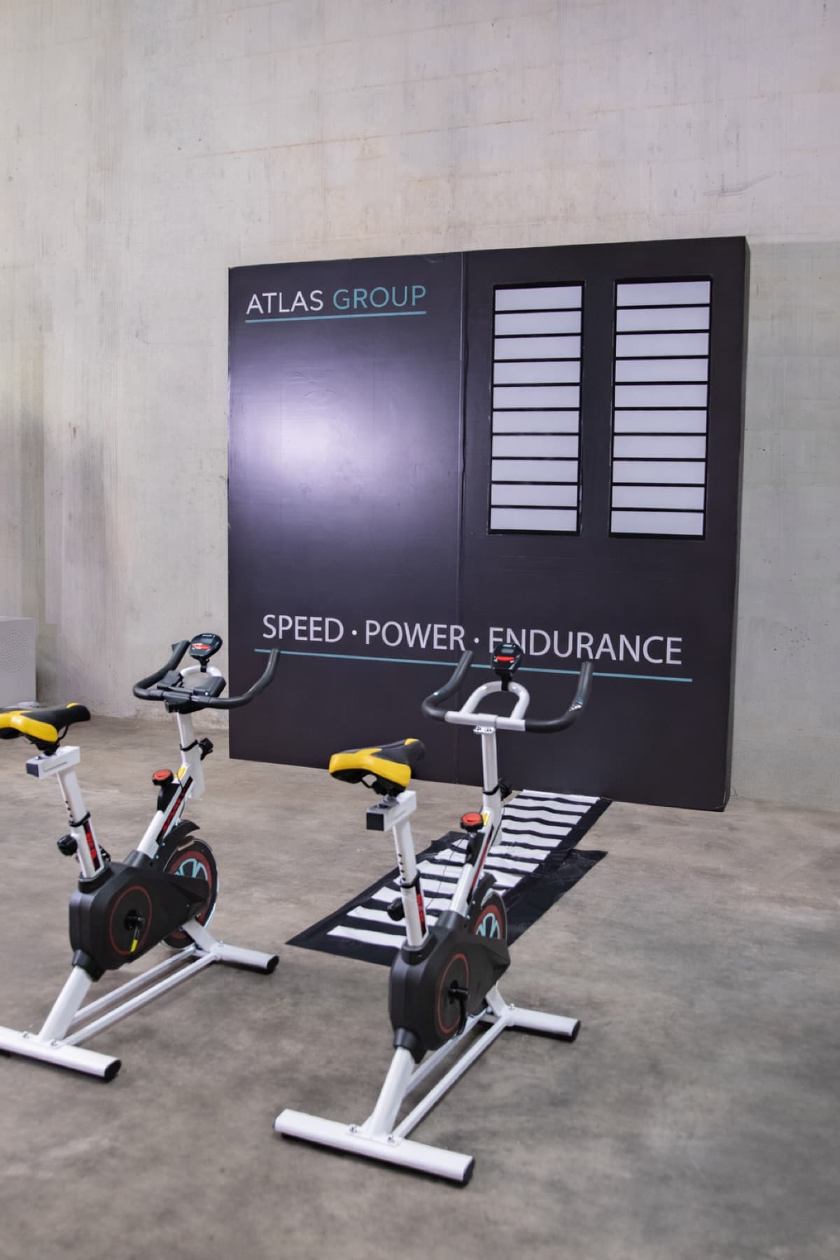 Two stationary bikes facing a branded speed, power, and endurance challenge wall